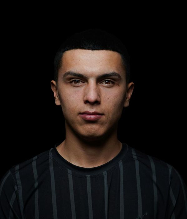 A man standing in a powerful but calm pose against a dark, minimalist background.